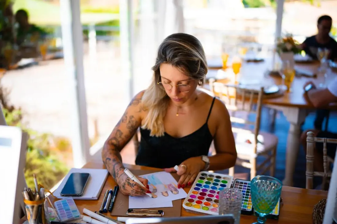 A Maria a pintar uma ilustração à mesa, com a paleta de aguarelas aberta, durante uma festa