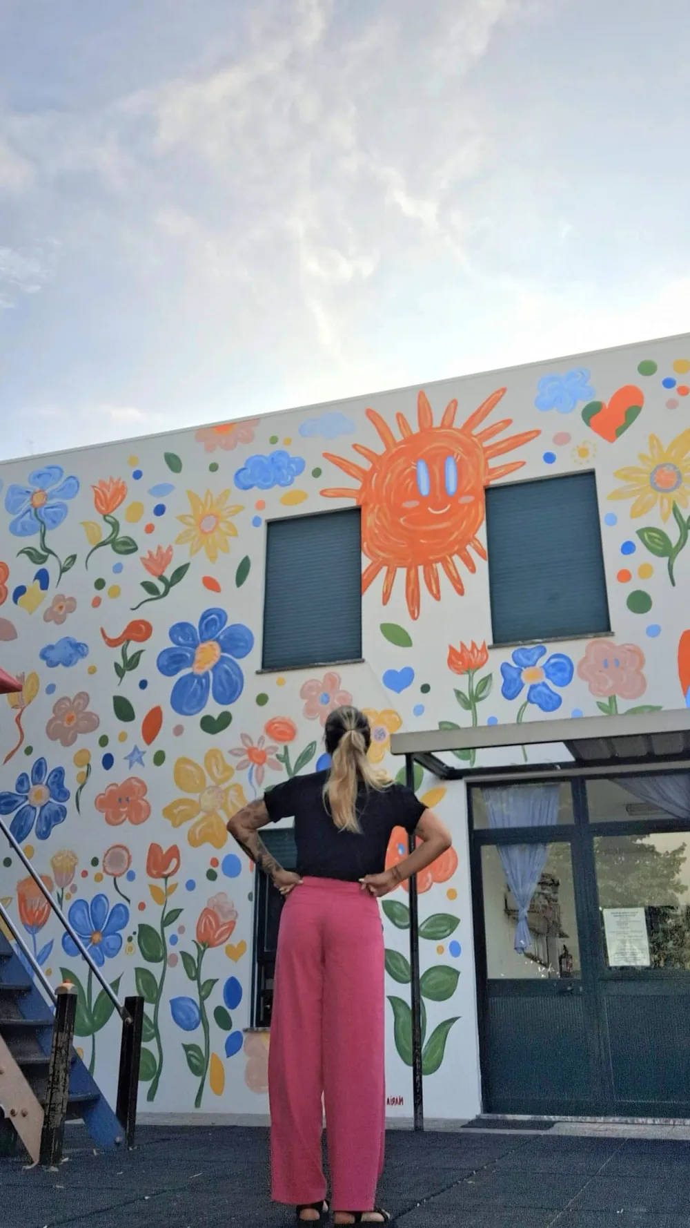 A Maria em frente ao mural de flores e sol que pintou numa escola